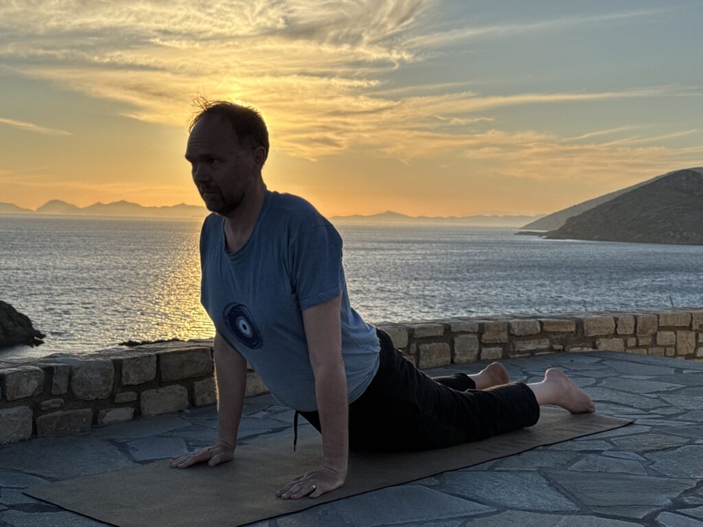 Martin Merz in der Haltung Kobra, bhujangasana. Im Hintergrund ein Sonnenuntergang mit Blick auf das Meer.