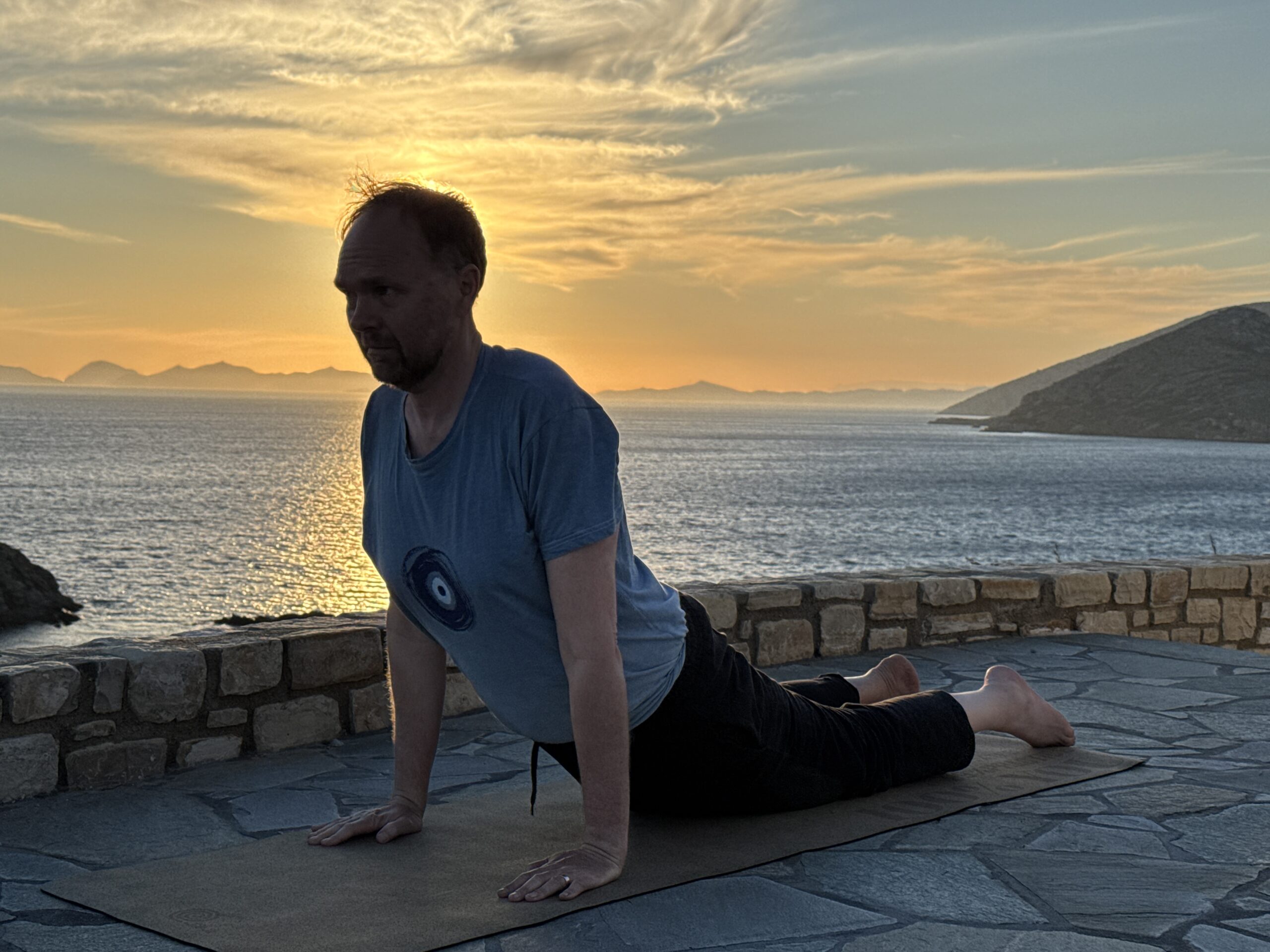 Martin Merz in der Haltung Kobra, bhujangasana. Im Hintergrund ein Sonnenuntergang mit Blick auf das Meer.